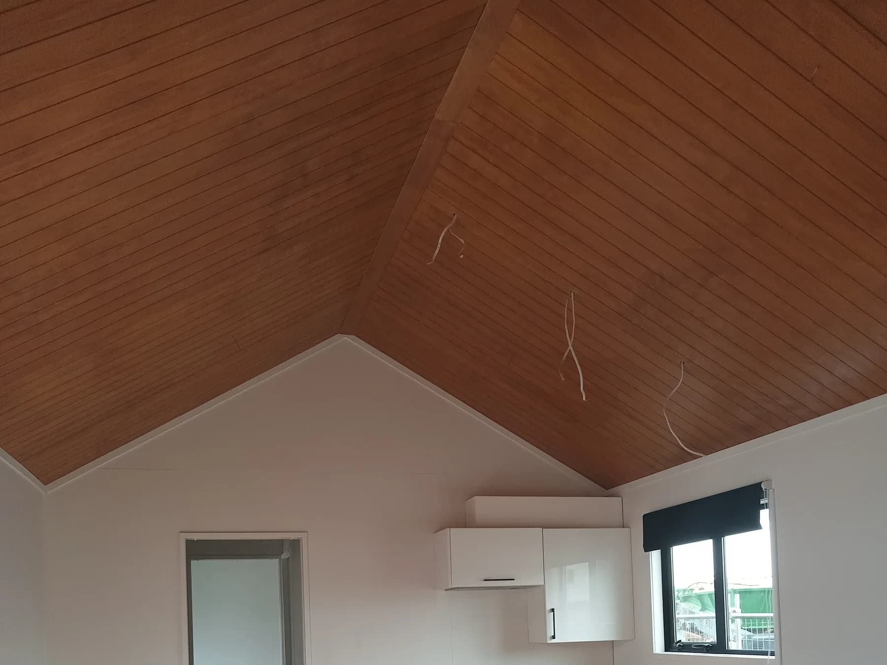 Vaulted apex ceiling lined in timber, with a heat pump and window beyond