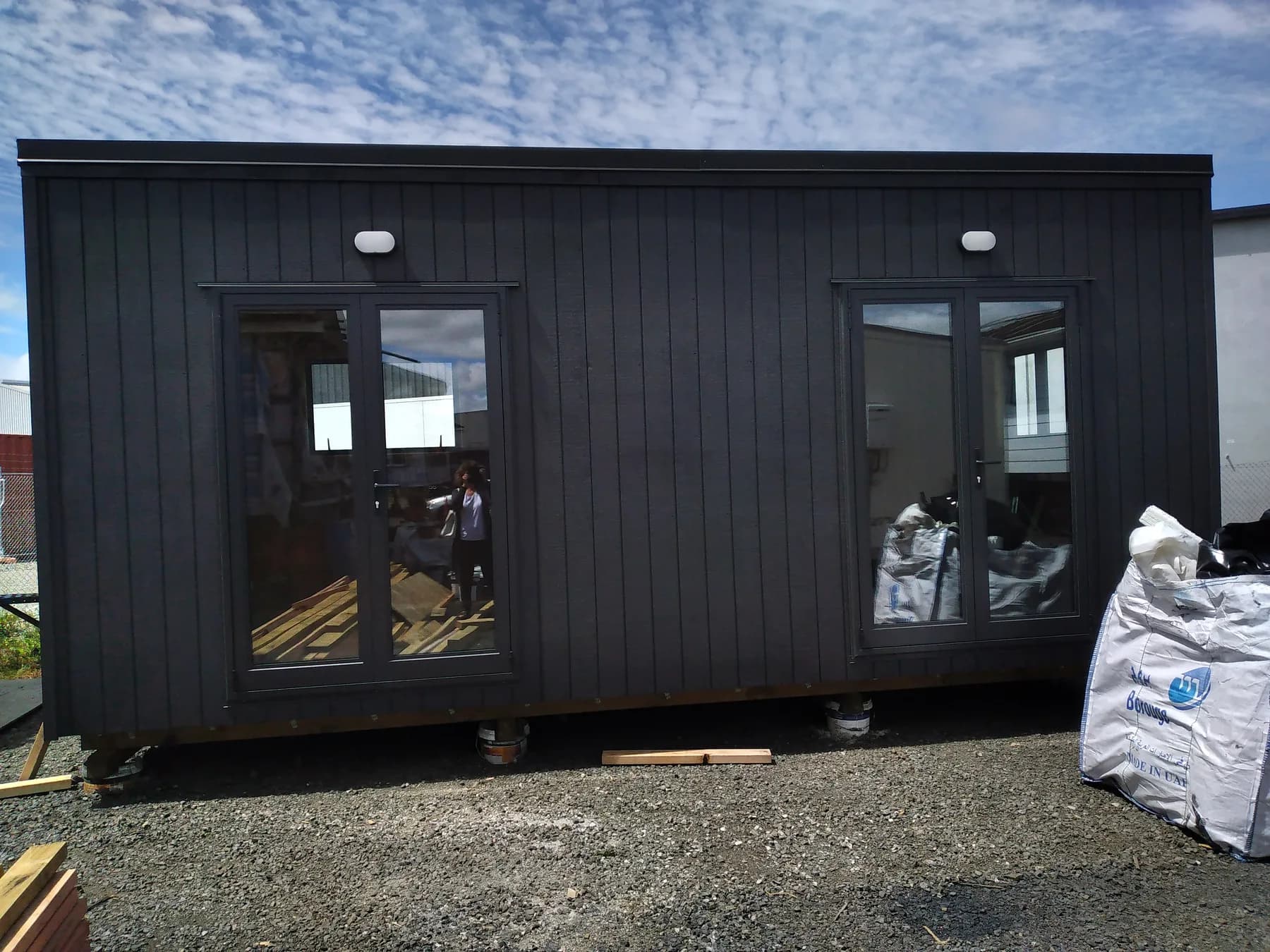 Dark-clad cabin on site with materials still stacked alongside